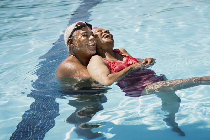 An adult African American couple swims in a pool on a hot day.