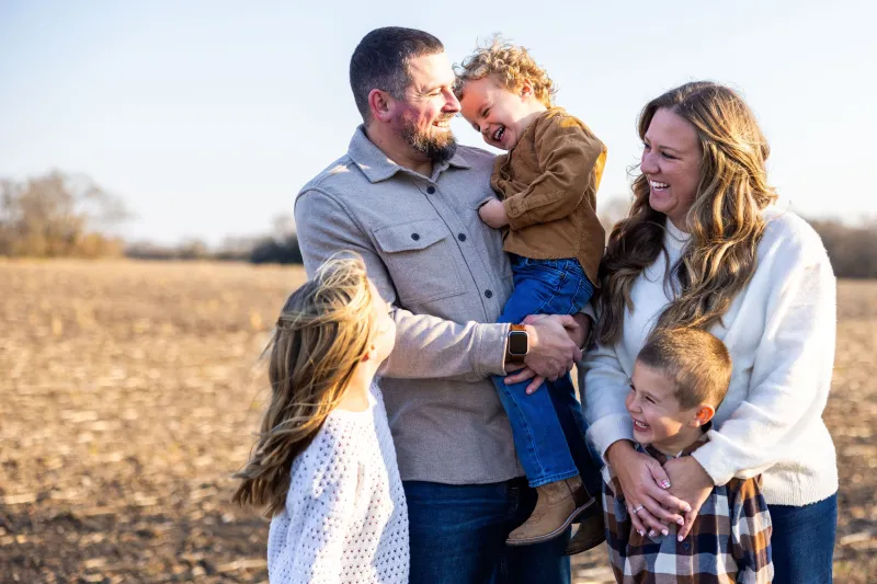 Husband and wife with their three kids, smiling and standing together in an empty field